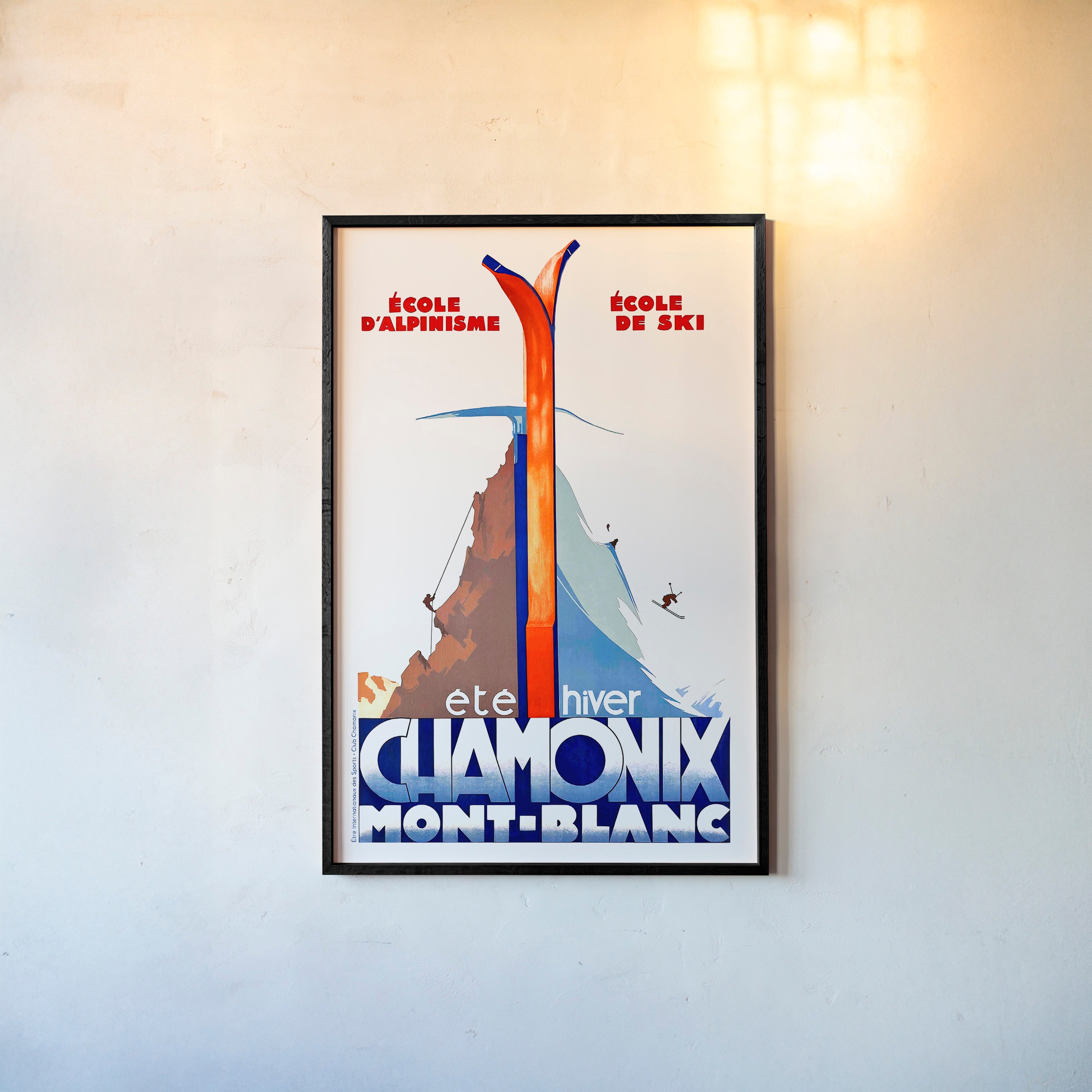 Framed poster of a mountain divided by a winter and summer scene with the text "Chamonic Mont-Blanc" at the bottom hanging in a light background