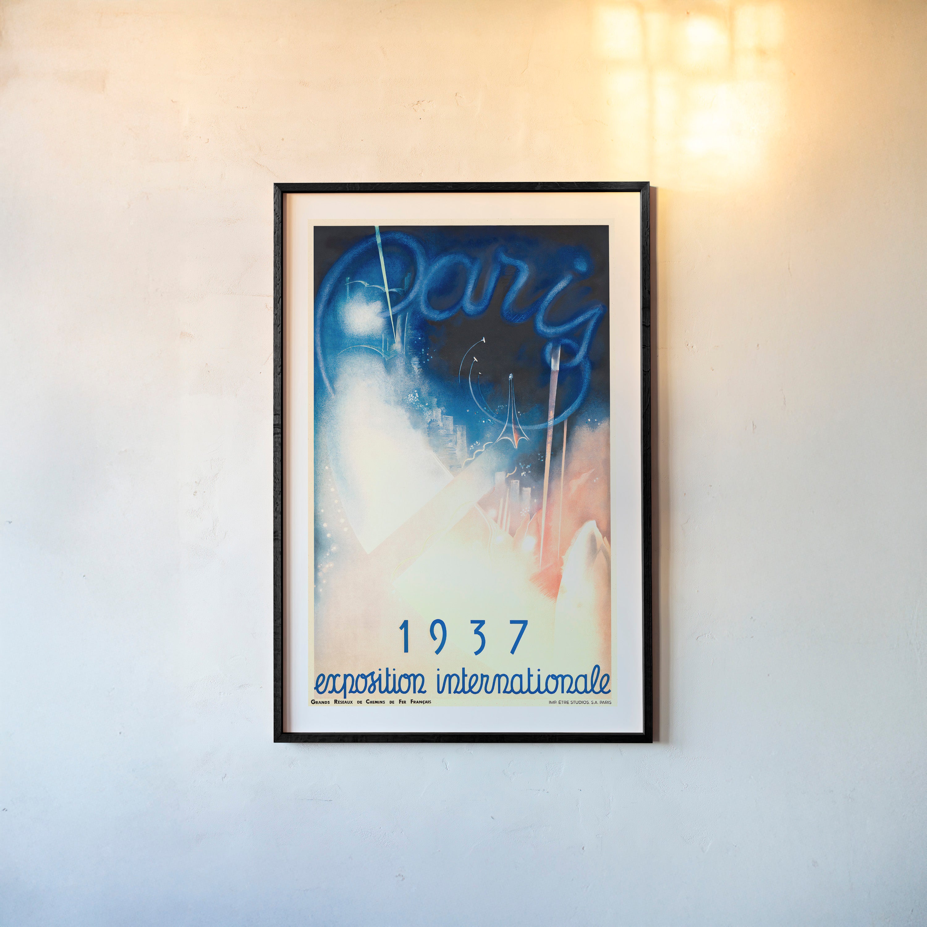 Framed poster of a whimsical blue and pink Paris scene with the text "1937 exposition internationale" at the bottom hanging on a light background
