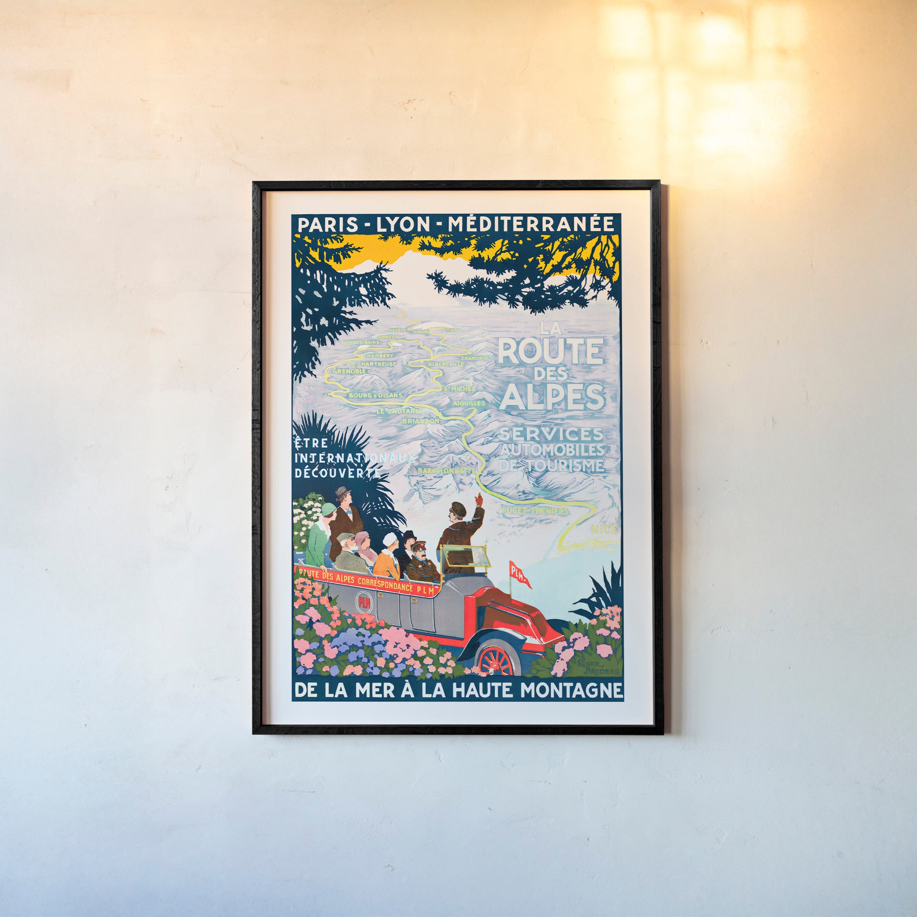 Framed poster featuring a map through the mountains and a tour guide with the text "La Route Des Alpes" at the center hanging on a light background