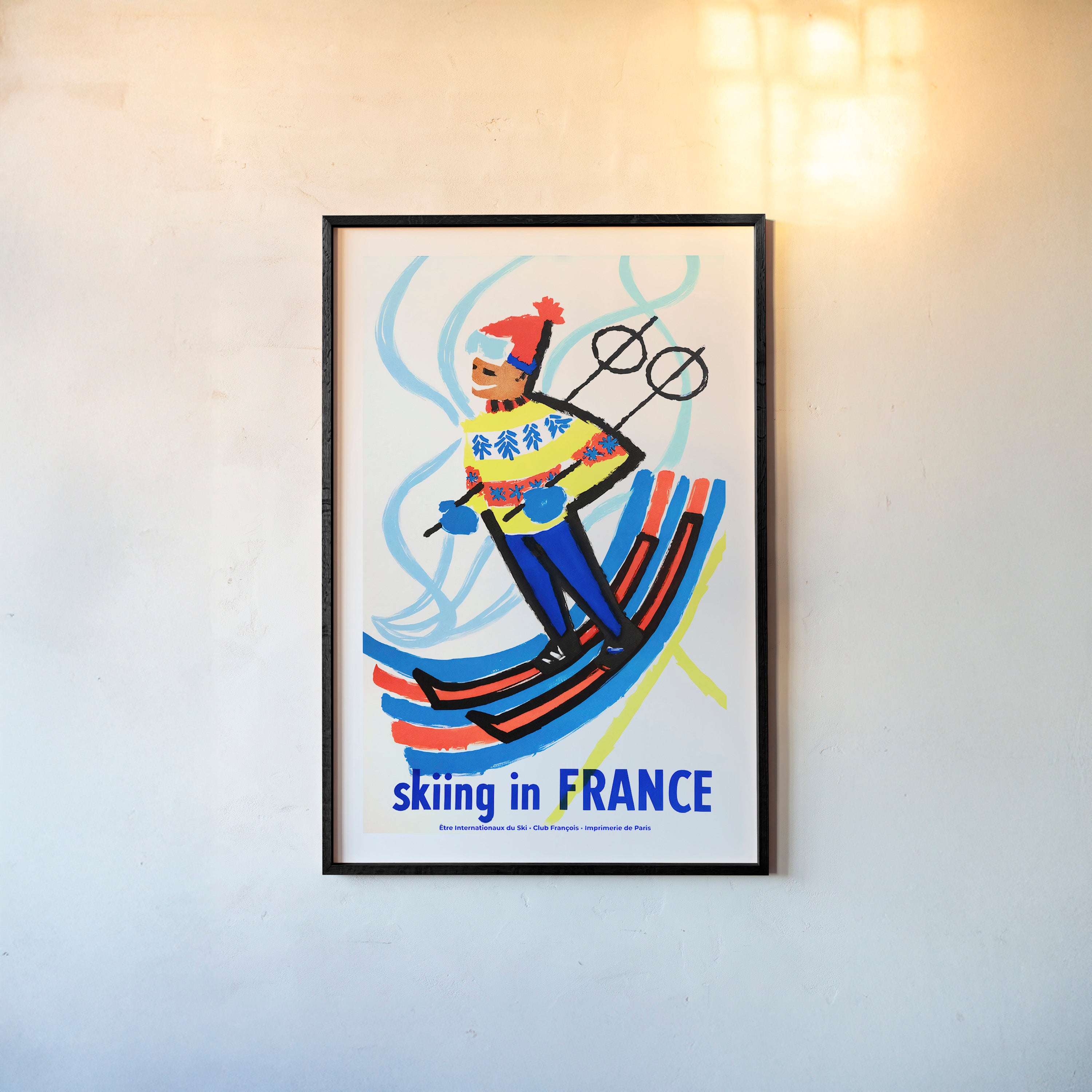 Framed poster of a skier with 'Skiing in France' text on a wall.