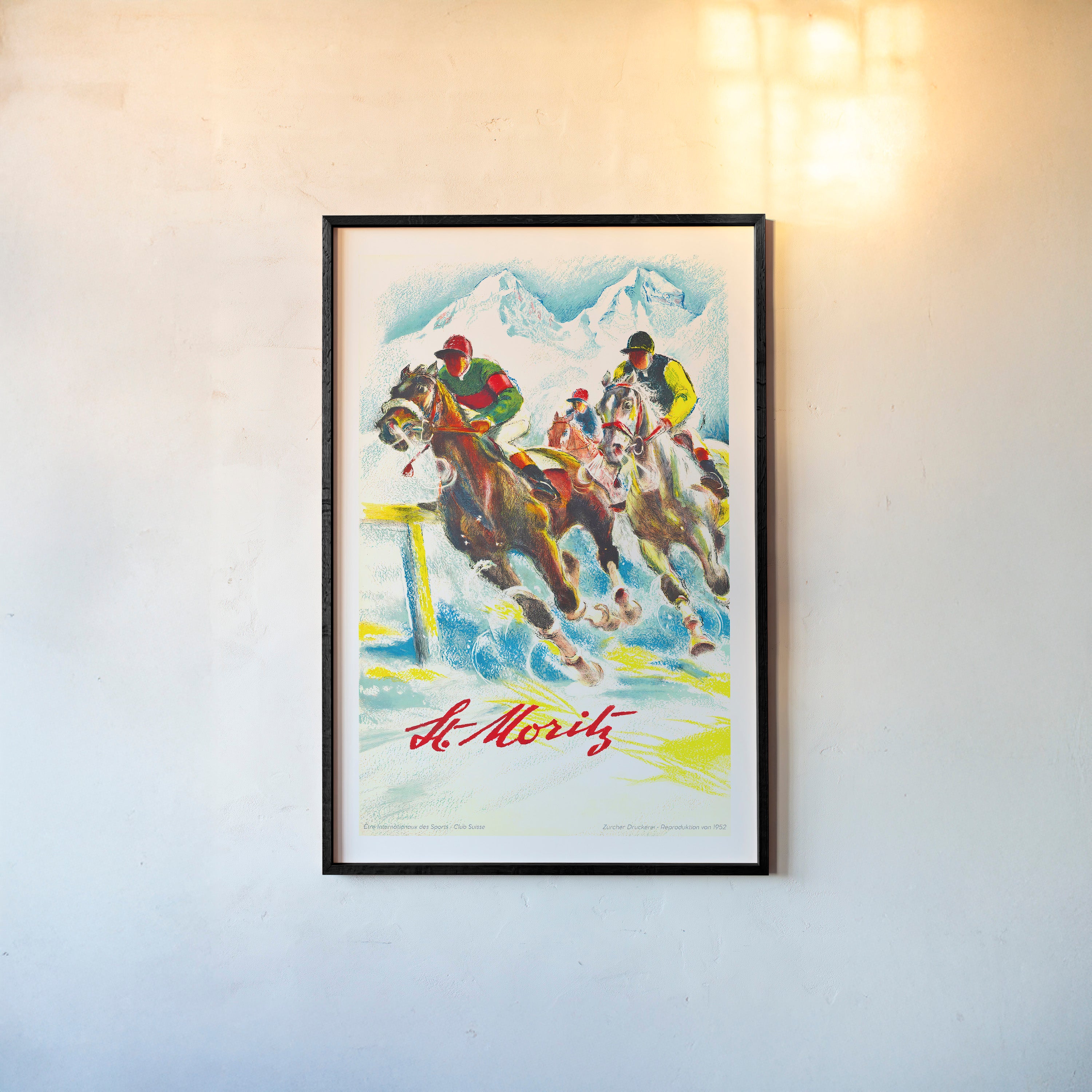 Framed poster of horse racers in the mountains with the text "St.Moritz" at the bottom hanging on a light background