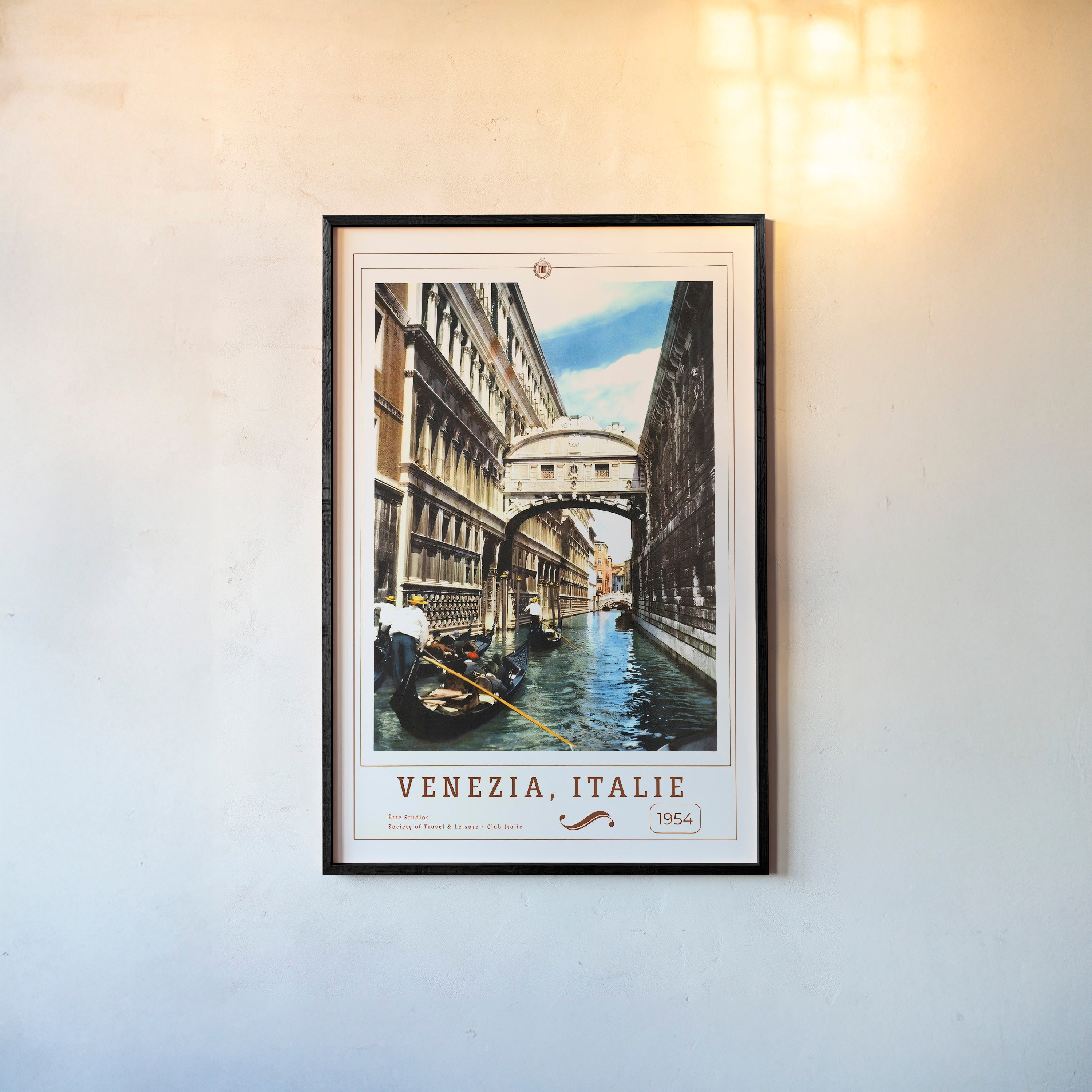 Framed poster of people on boats in a canal in between buildings with the text "Venezia, Italie" in large hanging on a wall with a light background
