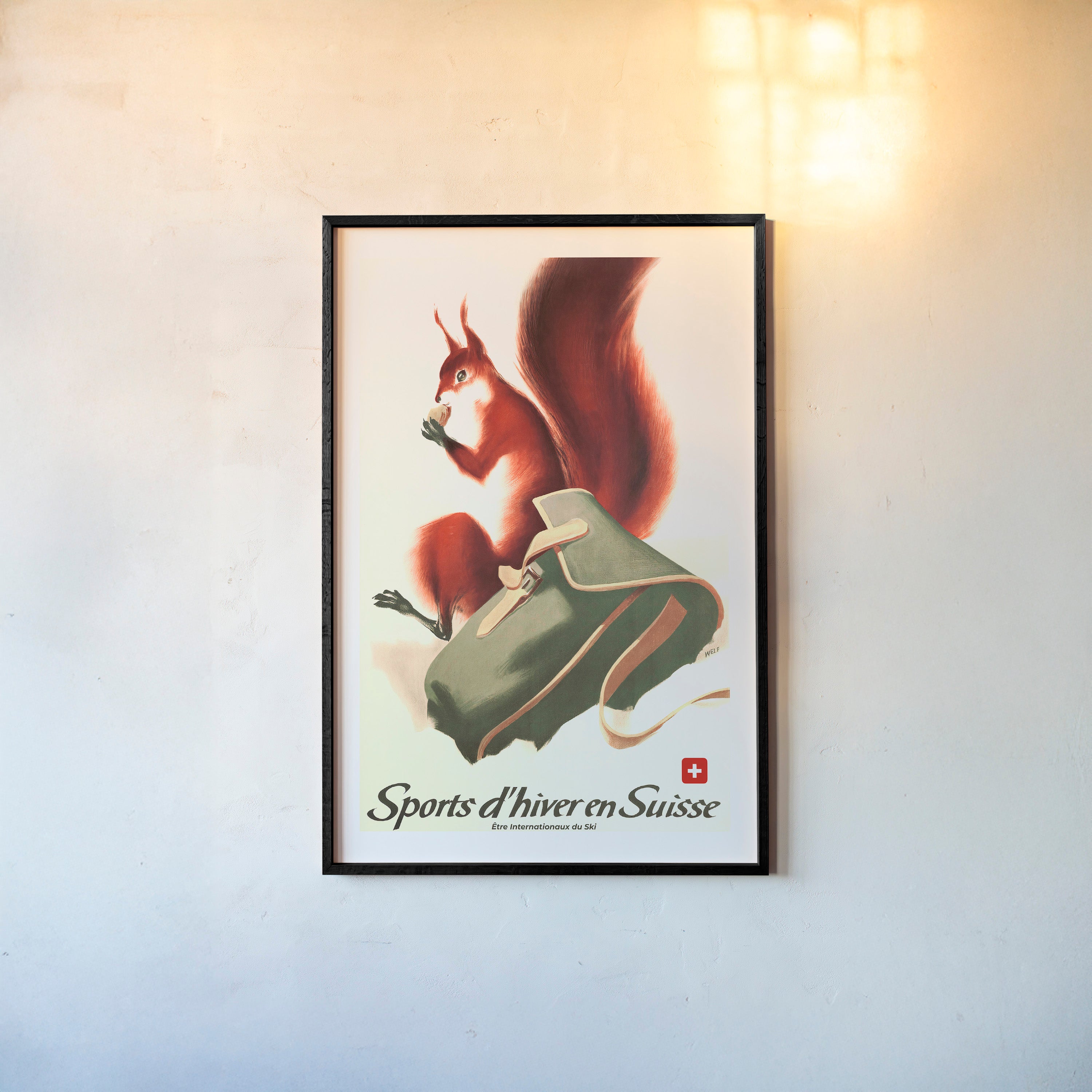 Framed poster of a fox next to a backpack in the snow with the text "Sports d'hiver en Suisse" at the bottom hanging on a wall with a light backdrop