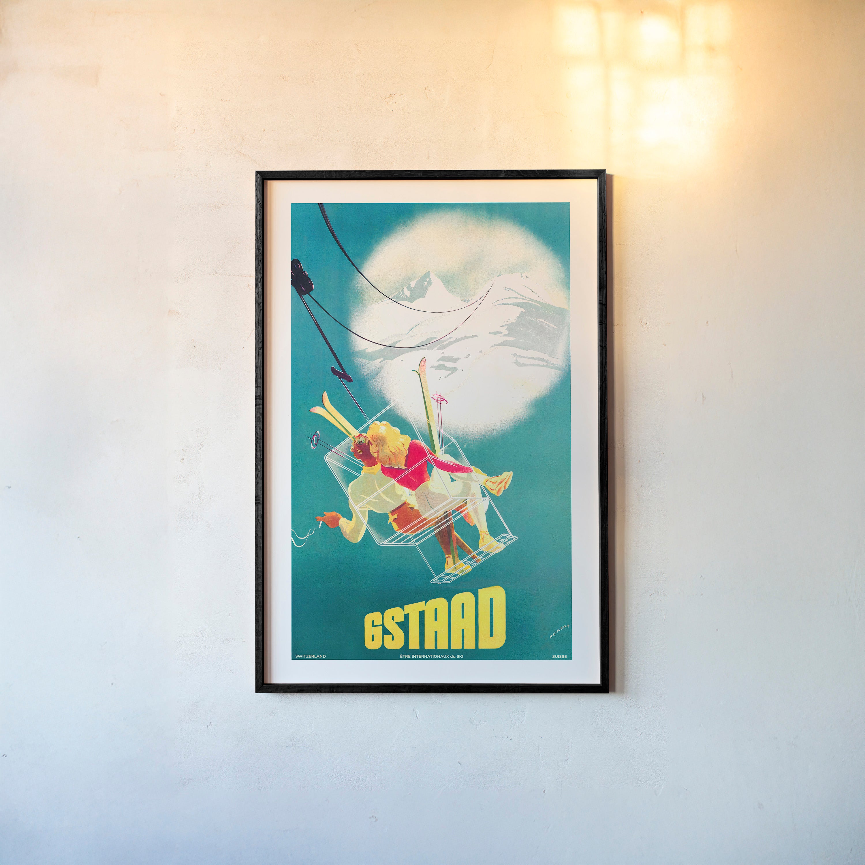 Framed poster of a whimsical ski lift image featuring two people and the text "GSTAAD" at the bottom hanging with a light background